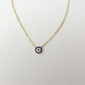 May include: A gold chain necklace with a small blue and white evil eye pendant. The pendant is surrounded by small white stones.