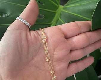 May include: A gold chain bracelet with three strands and small clear stones. The bracelet is on a person's wrist.