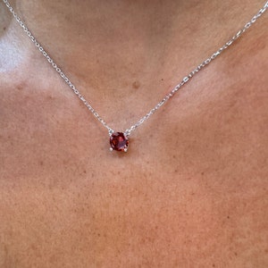 Peut inclure: Un collier en chaîne argent avec un pendentif rond en pierre rouge.