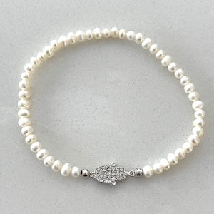 May include: A white pearl bracelet with a silver hamsa charm encrusted with clear rhinestones.