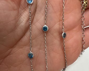 May include: A silver chain necklace with blue gemstones. The necklace has a delicate chain and round blue stones.