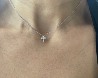 May include: A delicate silver chain necklace with a small, diamond-encrusted cross pendant.