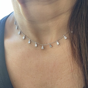 May include: A silver necklace with a delicate chain and pear-shaped clear stones hanging from it.