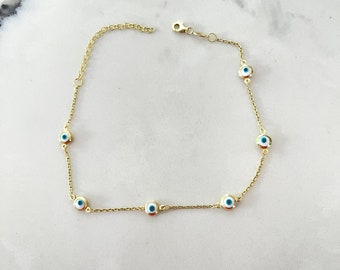 May include: A gold chain anklet with five blue evil eye charms. The anklet has a lobster clasp closure.