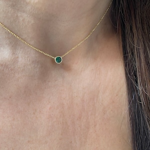 May include: A delicate gold chain necklace with a small, round, dark green gemstone pendant.