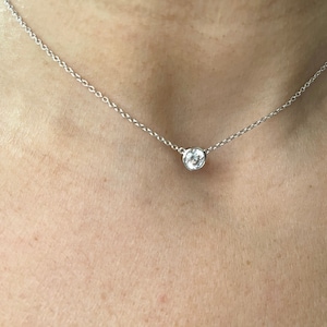 May include: A simple silver chain necklace with a single round clear gemstone pendant.