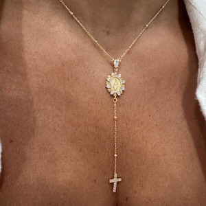 May include: Gold-toned necklace featuring a pendant with a religious motif, surrounded by sparkling accents. The necklace has a delicate chain with a cross pendant at the end. The design is elegant and suitable for religious occasions.