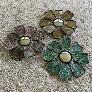 May include: Three decorative flower-shaped mirrors with mosaic tile designs. The mirrors are in shades of pink, yellow, and blue.