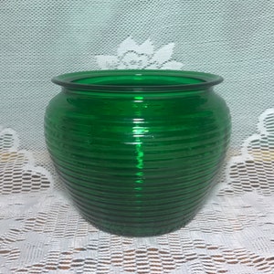 May include: A vivid green glass vase with a rounded, ribbed design. The vase features a wide opening and a dark green rim. The glass reflects light, accentuating the horizontal ridges. A decorative item for home decor.