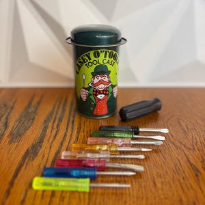 May include: A vintage Casey O'Tool Tool Case with a green lid and a cartoon image of a man in a suit. A set of colorful screwdrivers with clear handles and metal tips are arranged on a wooden surface.