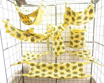 Puede incluir: Un conjunto de accesorios para jaula de hámster de color amarillo y gris con un patrón de panal. El conjunto incluye una hamaca, un juguete colgante, un escondite y una plataforma.