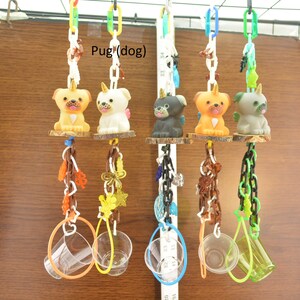 May include: A collection of colorful dog-themed hanging toys. Each toy features a pug figurine with a unicorn horn, suspended from a chain. The toys are attached to wooden platforms and adorned with various decorative elements, including plastic rings and chains.