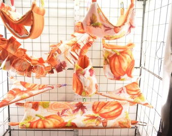 May include: A set of seven orange and white pumpkin-themed hanging hamster cage accessories. The accessories include a hammock, a hanging pouch, a hanging tunnel, a hanging platform, and a hanging toy.