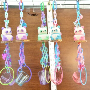 May include: A collection of colorful bird toys featuring panda-unicorn figures. Each toy has a panda figurine with a unicorn horn, wings, and a small wooden perch. The toys are suspended by chains and include hanging rings and cups.
