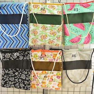 Puede incluir: Colección de seis bolsas de mano con varios diseños. Los diseños incluyen chevrones azules, monos, sandías, flores, búhos y gris liso. Cada bolsa tiene un panel de malla en contraste y una correa blanca o negra.