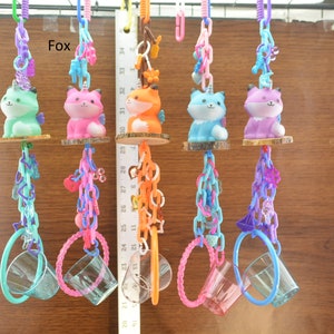 May include: A collection of colorful fox-themed hanging toys. Each toy features a fox figurine in various colors, suspended by chains and connected to a clear cup. The word "Fox" is visible in the image.