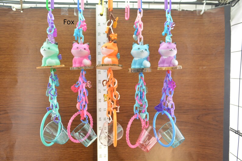 May include: A collection of colorful fox-themed hanging toys. Each toy features a fox figurine in various colors, suspended by chains and connected to a clear cup. The word "Fox" is visible in the image.