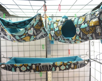 May include: Three hanging pet beds with a wintery woodland print. The beds are made of a soft, blue fabric with a dark gray background and feature a variety of woodland creatures, trees, and snowflakes. The beds are designed to hang from a cage or other structure.