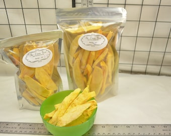 May include: Two clear plastic bags filled with dried mango slices. The bags have a white label with the text "The Lemon Rose" and "Mango, 1 lb". A small green bowl with dried mango slices is in the foreground.