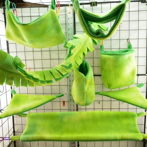 May include: A set of green fleece pet hammocks and toys for small animals. The set includes a hammock, a hanging toy, a pouch, and a tunnel.