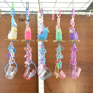 May include: A collection of colorful llama-themed bird toys. Each toy features a small llama figure in various colors, suspended by chains and a clear plastic cup. The word "Llama" is visible in the image.