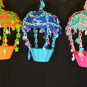May include: Three colorful hanging bird toys with different colored plastic cups and chains of beads and charms. The toys are made of plastic and are designed to be hung from a bird cage.