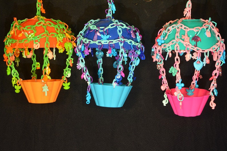 May include: Three colorful hanging bird toys with different colored plastic cups and chains of beads and charms. The toys are made of plastic and are designed to be hung from a bird cage.