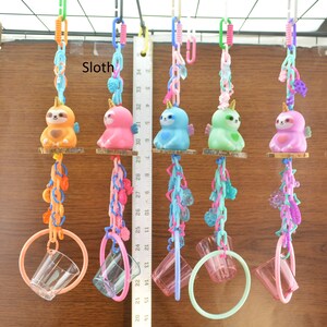 May include: A collection of colorful sloth-shaped toys with wings, each hanging from a chain and a ring. The sloths are in various colors, including orange, pink, blue, green, and purple. The word "Sloth" is visible in the image.