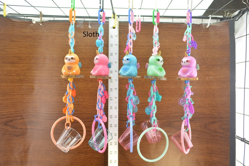 May include: A collection of colorful sloth-shaped toys with wings, each hanging from a chain and a ring. The sloths are in various colors, including orange, pink, blue, green, and purple. The word "Sloth" is visible in the image.