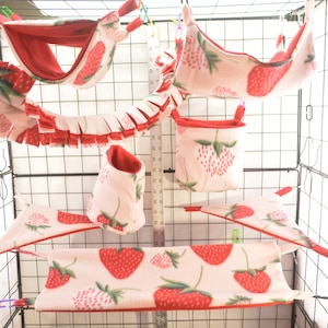 Puede incluir: Un conjunto de seis hamacas colgantes con estampado de fresas y una bolsa colgante para mascotas pequeñas. Las hamacas están hechas de tela polar suave de color rosa y rojo con estampado de fresas. La bolsa está hecha de la misma tela y tiene un forro de polar rojo.