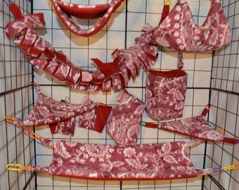Puede incluir: Un conjunto de hamacas y juguetes colgantes de tela roja y blanca con estampado para mascotas pequeñas. Los artículos están hechos de tela suave y afelpada y están diseñados para colgarse dentro de una jaula.