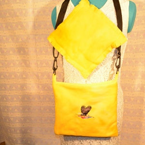 May include: A yellow fabric crossbody bag with a black strap and an embroidered eagle design. The bag has a smaller yellow fabric pouch attached to the strap.
