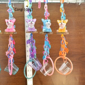 May include: Colorful hanging pet toys featuring corgi dog figurines with unicorn horns and wings. Each toy has a clear plastic cup and a ring, connected by chains in various colors like teal, pink, purple, and orange.