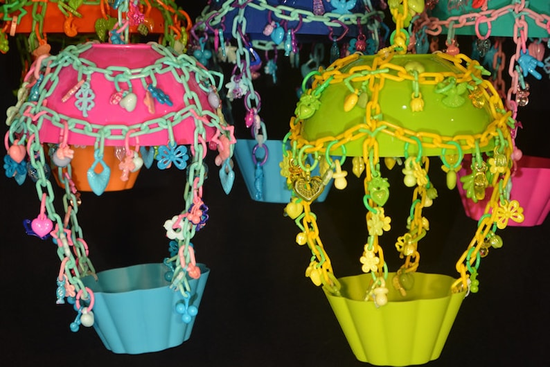 May include: Four colorful hanging bird toys with different colored plastic bowls and chains with various plastic charms. The bowls are pink, green, blue, and orange.