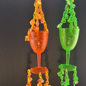 May include: Two plastic cups with chains and charms hanging from them. The cup on the left is orange and the cup on the right is green.