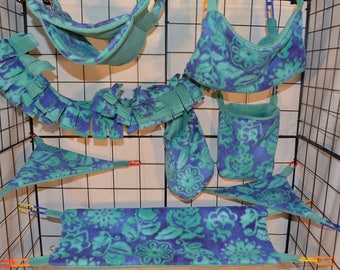 Puede incluir: Un conjunto de hamacas de tela con estampado azul verdoso y morado, juguetes colgantes y un túnel de forro polar para mascotas pequeñas. Los artículos están colgados en una jaula de alambre.