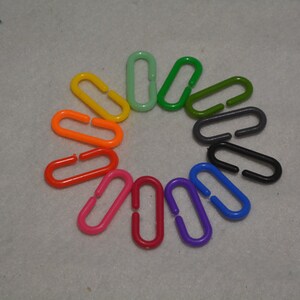 Puede incluir: Un conjunto de 12 anillos ovalados de pl&aacute;stico de colores vivos con una peque&ntilde;a abertura en el centro. Los anillos est&aacute;n dispuestos en c&iacute;rculo, con colores que van del verde al naranja, del rojo al morado.