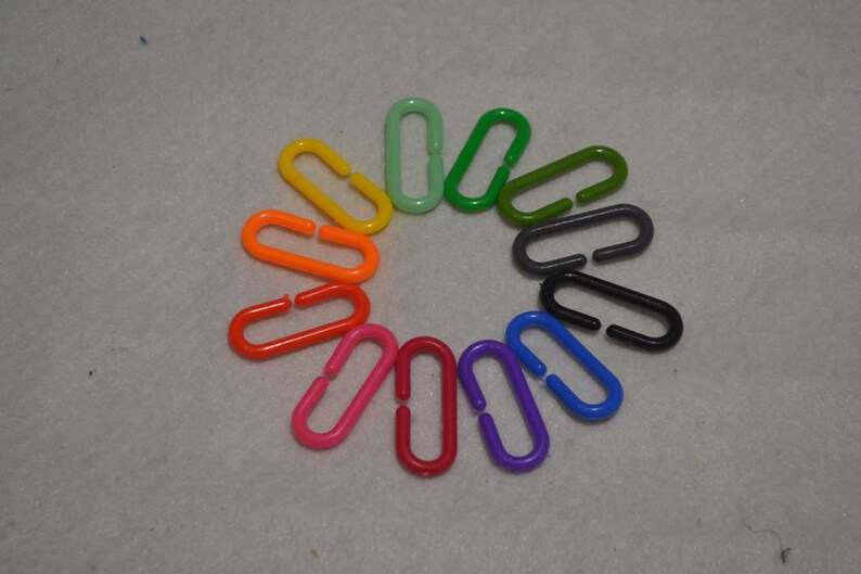 Puede incluir: Un conjunto de 12 anillos ovalados de pl&aacute;stico de colores vivos con una peque&ntilde;a abertura en el centro. Los anillos est&aacute;n dispuestos en c&iacute;rculo, con colores que van del verde al naranja, del rojo al morado.