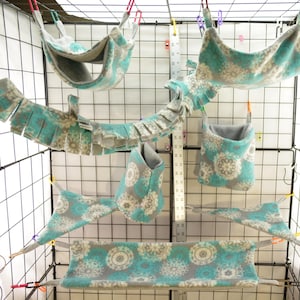 May include: A set of fleece pet accessories in a teal and gray floral pattern, including hammocks, a tunnel, a pouch, and a bridge. A vertical ruler is visible, showing measurements in inches, with the largest hammock spanning 14 inches wide.