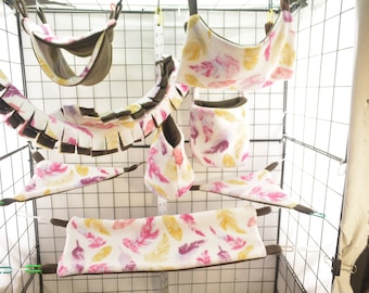 May include: A set of colorful hanging hammocks and tunnels for small pets, featuring a white fabric with a pink, purple, and yellow feather pattern. The hammocks are made of soft, plush fabric and are perfect for providing a cozy and comfortable space for your pet to relax and play.