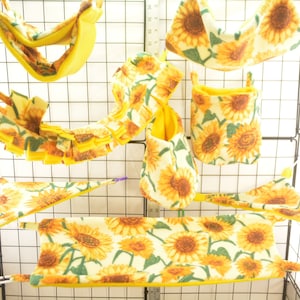 May include: A set of sunflower-patterned hanging hammocks and pouches for small animals. The cage is made of wire and has a yellow and white colour scheme.