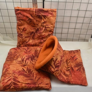 May include: A set of three pet bedding items. The items include a rectangular bed, a tunnel, and a pillow. The items are orange with a leaf pattern and an orange fleece interior. The items are designed for small pets.
