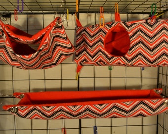 May include: Three red and black chevron patterned hanging beds for small pets. The beds are made of soft fabric and have a red fleece lining. The beds are attached to a wire cage with metal clips.