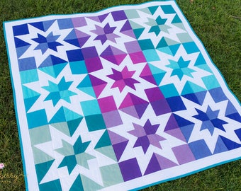 May include: A quilt with a starburst pattern in shades of blue, teal, purple, and white. The quilt is made of fabric squares sewn together to create a geometric design.