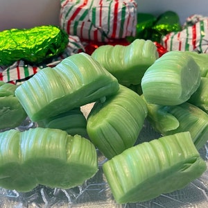 Puede incluir: Primer plano de un plato de caramelos de menta verde. Los caramelos están envueltos en celofán transparente y tienen una textura ligeramente ondulada.