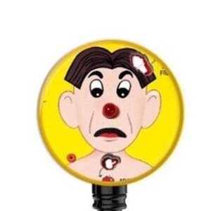 May include: A yellow badge reel featuring a cartoon image of a person with a red nose and a bandage on their head. The person is surrounded by red dots and the text "First Aid" is visible on the right side of the image.