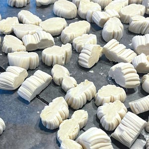 May include: A collection of off-white, textured, and uniquely shaped pieces, possibly handmade, scattered across a surface. The shapes vary, some resembling small, rounded forms, others more rectangular with ribbed edges.