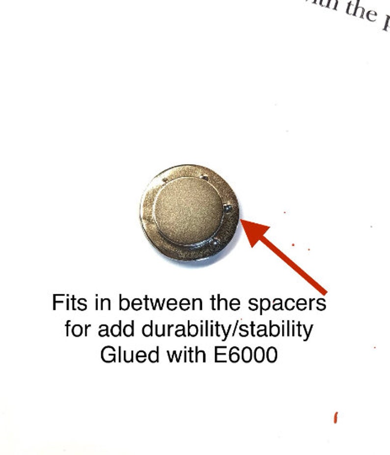 Pode incluir: Um disco de metal prateado com um centro elevado. O disco &eacute; projetado para caber entre os espa&ccedil;adores para maior durabilidade e estabilidade. O texto "Colado com E6000" est&aacute; escrito abaixo do disco.