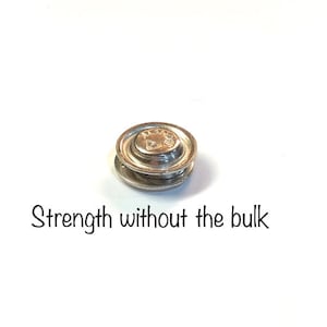 May include: A silver-colored magnetic clasp with a circular design. The clasp is composed of two stacked, round pieces. The text "Strength without the bulk" is below the clasp.