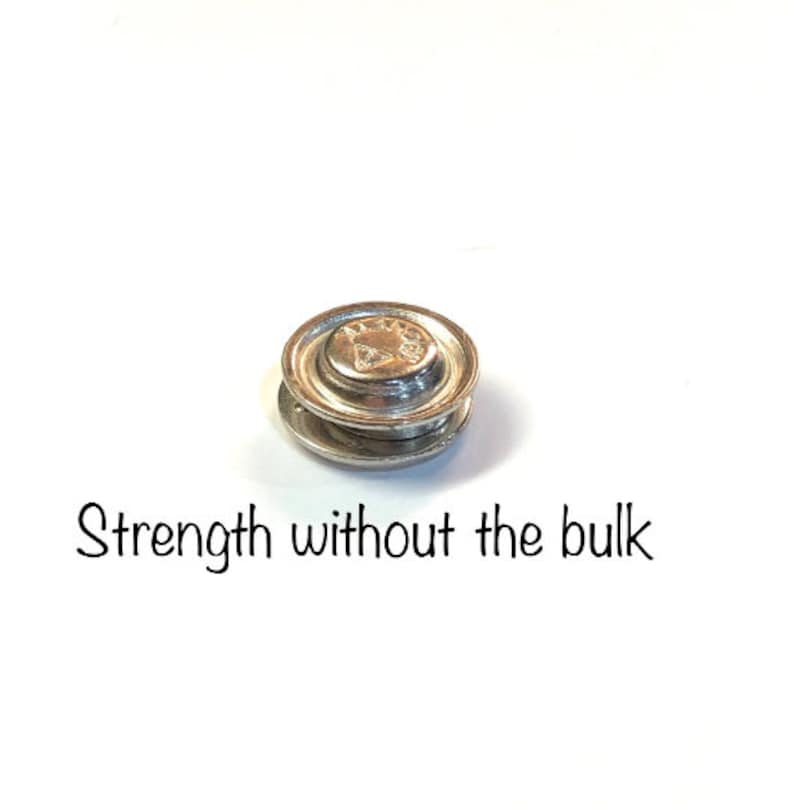 Pode incluir: Um fecho magn&eacute;tico de metal prateado, tamb&eacute;m conhecido como bot&atilde;o magn&eacute;tico, com as palavras "Strength without the bulk" impressas abaixo.